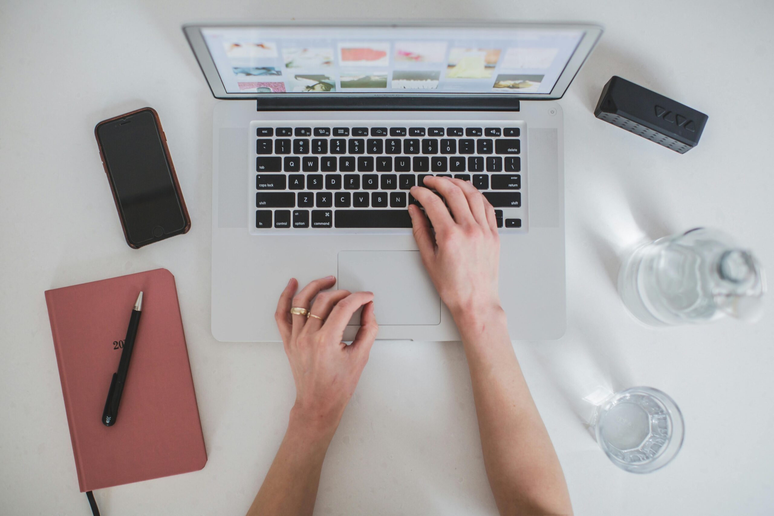  Administrative virtual assistants at work, depicted by a top-down view of hands typing on a laptop keyboard with an open planner and a smartphone on the side.