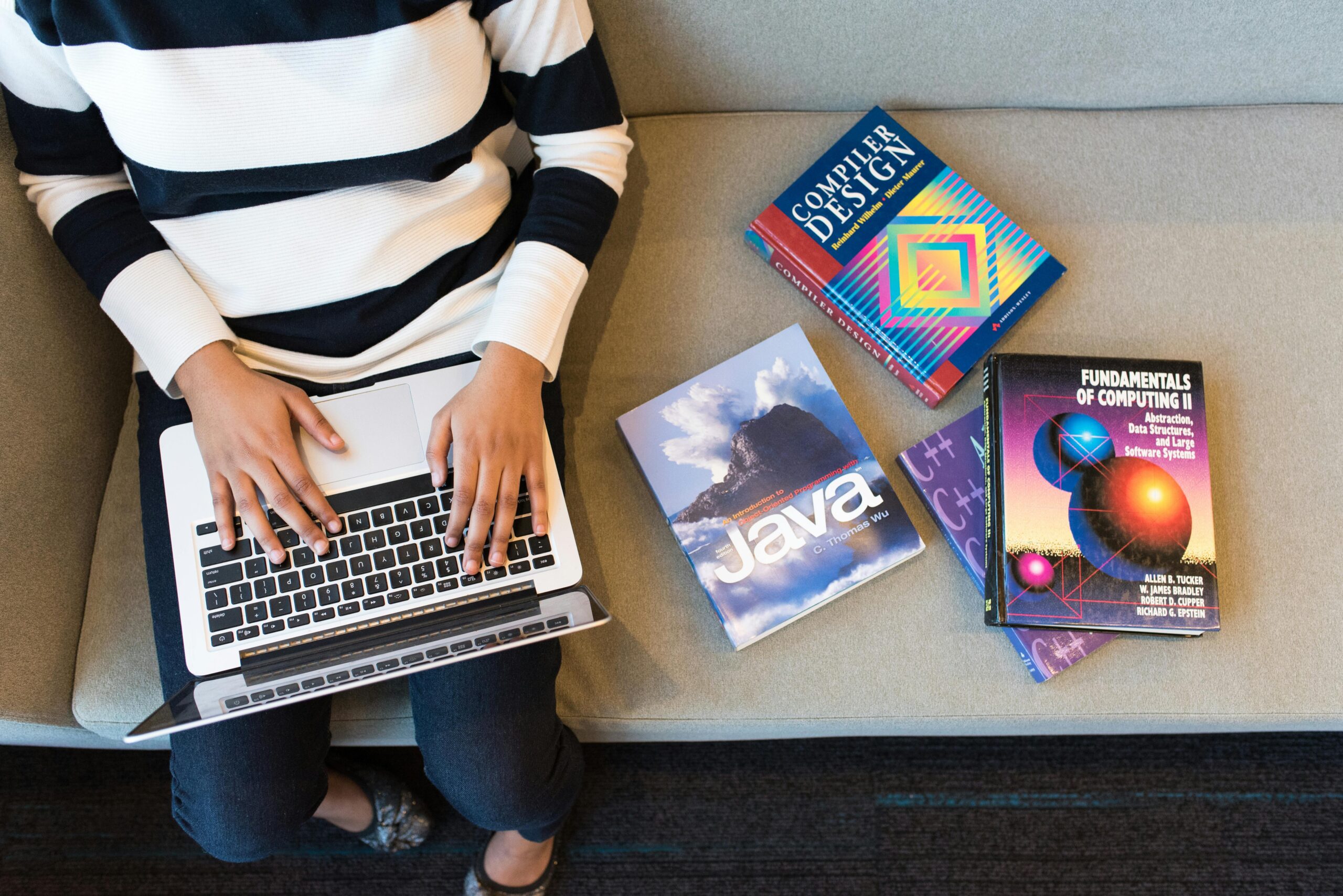 A student with textbooks on computer programming studying on a laptop.