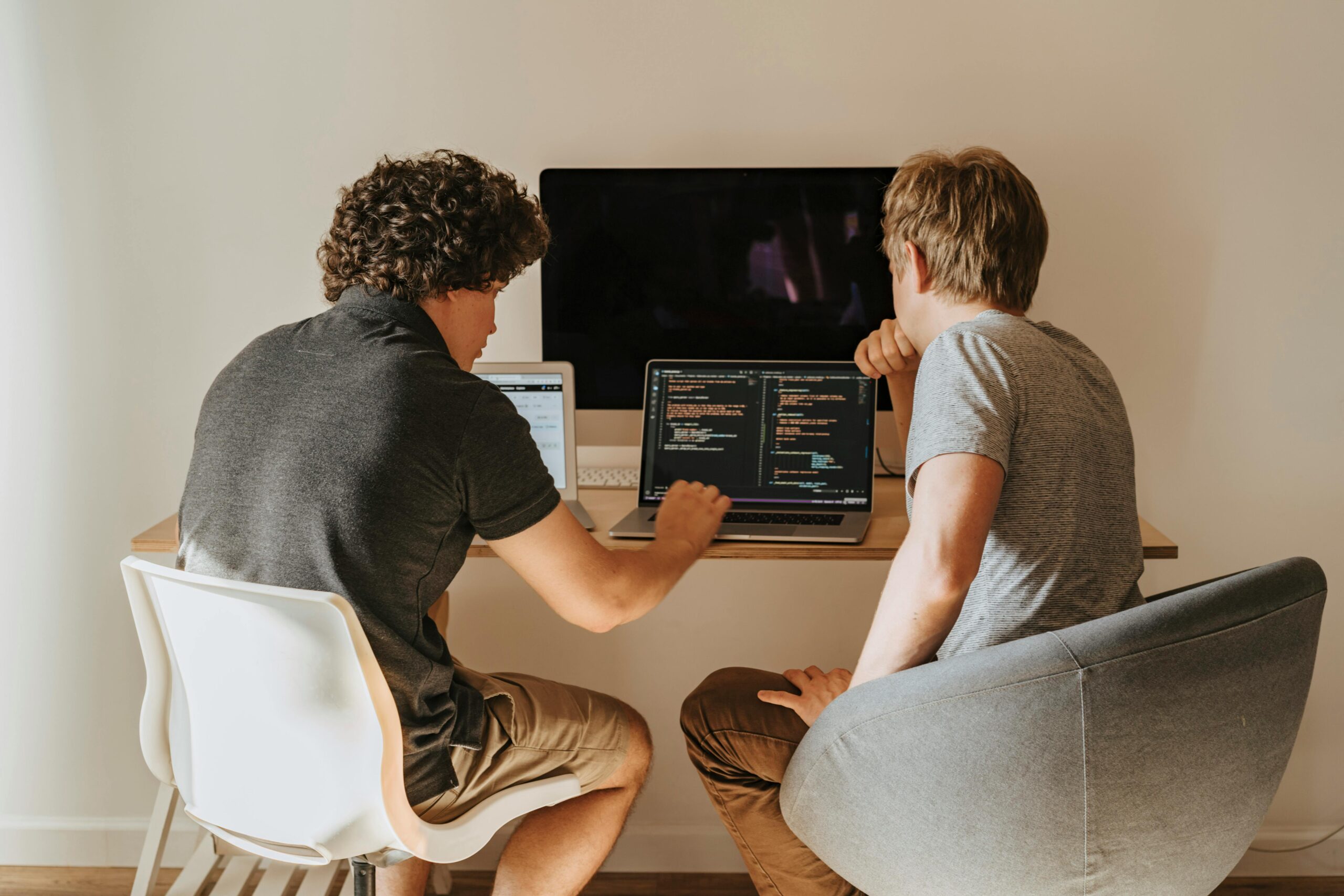 Two developers collaborating on a project with laptops and a desktop computer.
