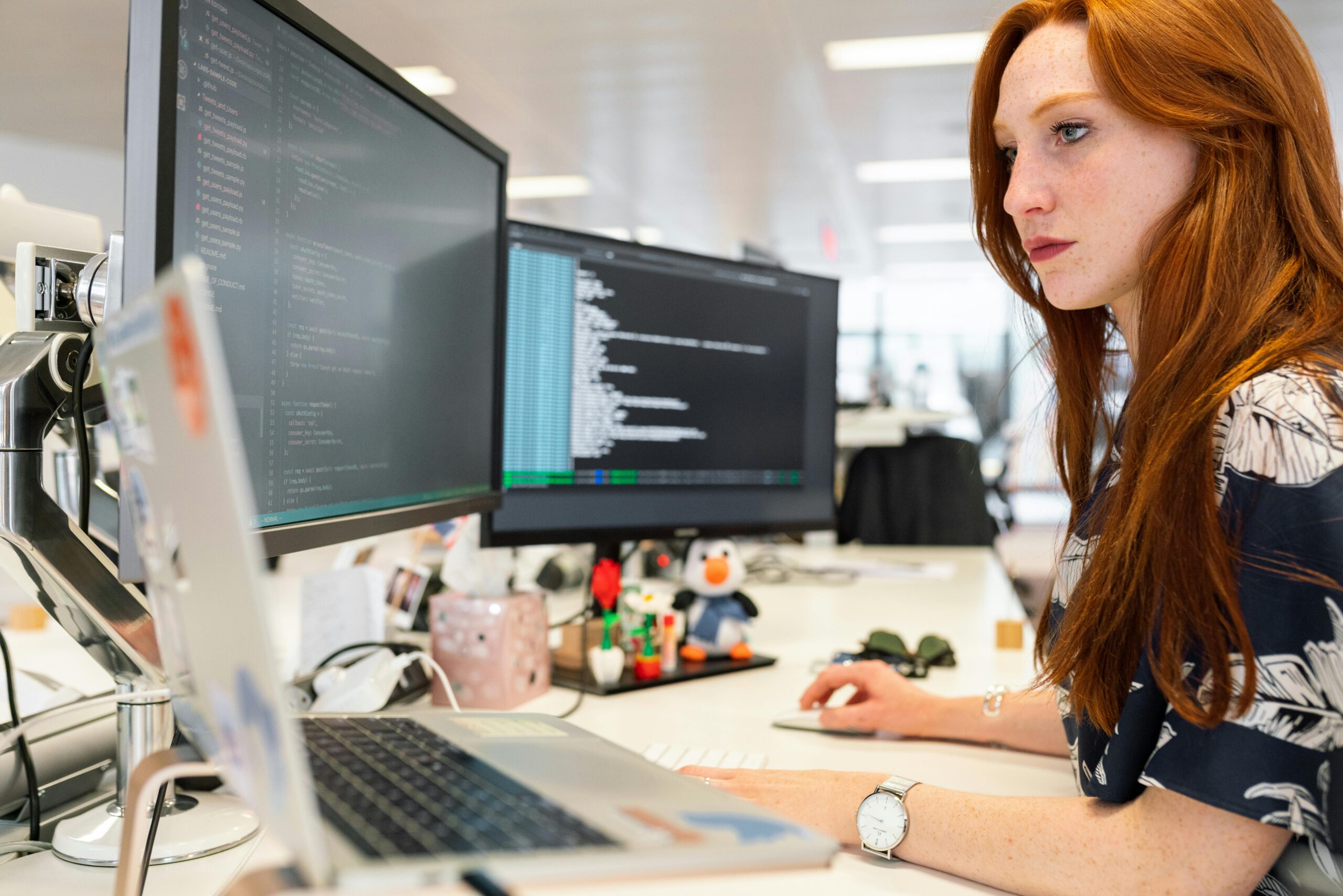 A programmer intensely coding on a laptop with a large desktop monitor displaying code.