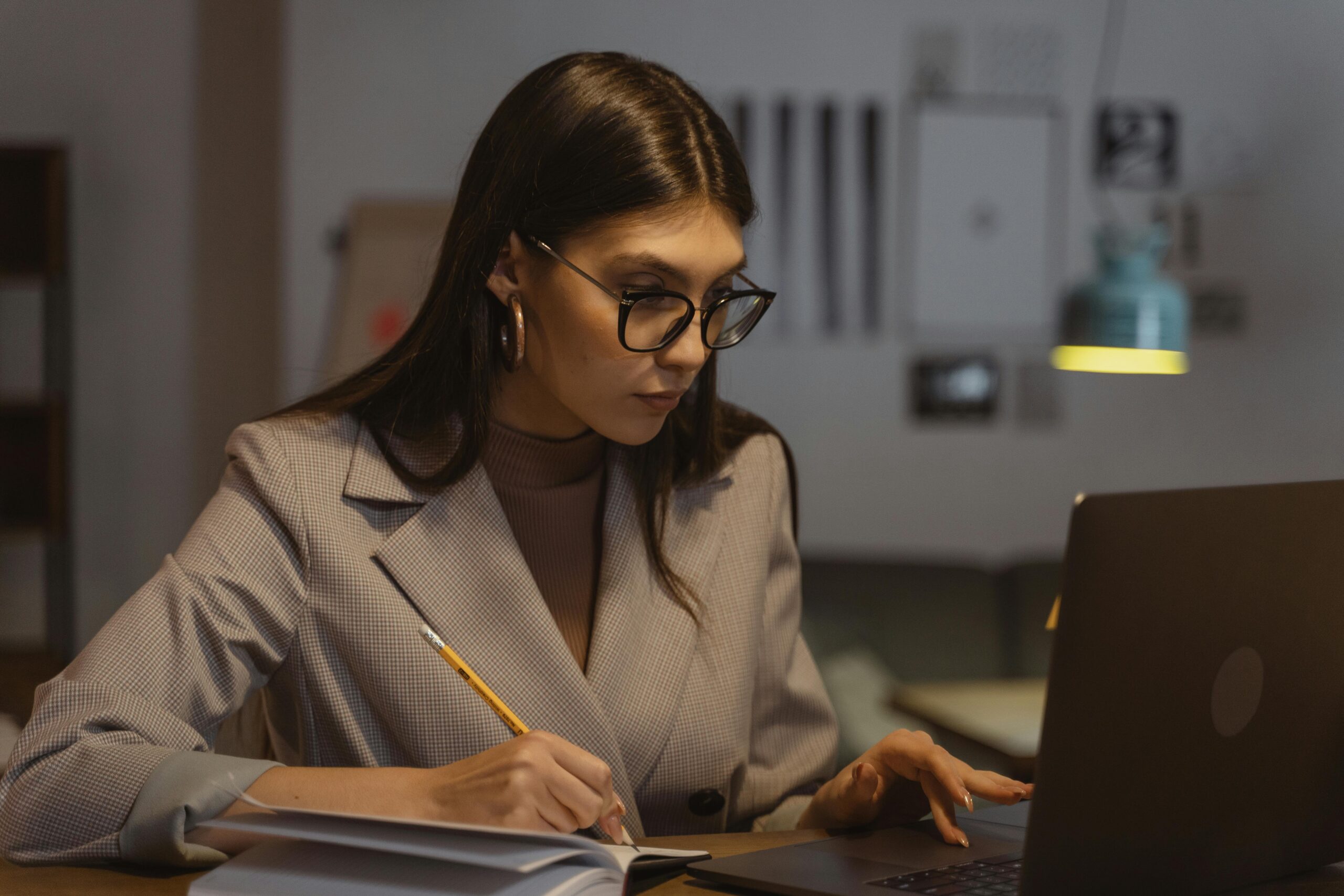 A person with their face obscured is sitting at a desk in a dimly lit room.