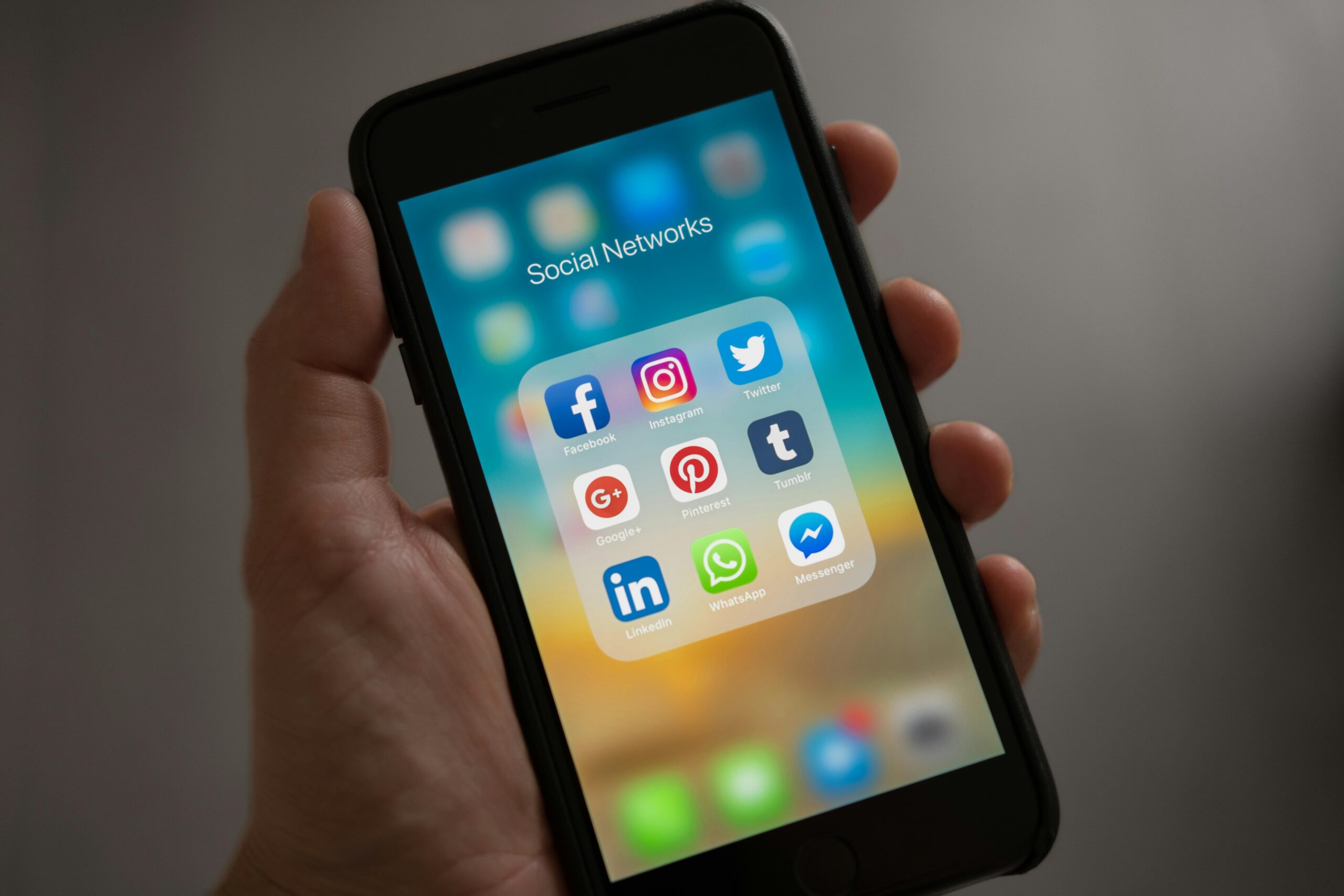 A person holding a smartphone with a screen displaying a folder labeled 'Social Networks' containing various social media app icons.