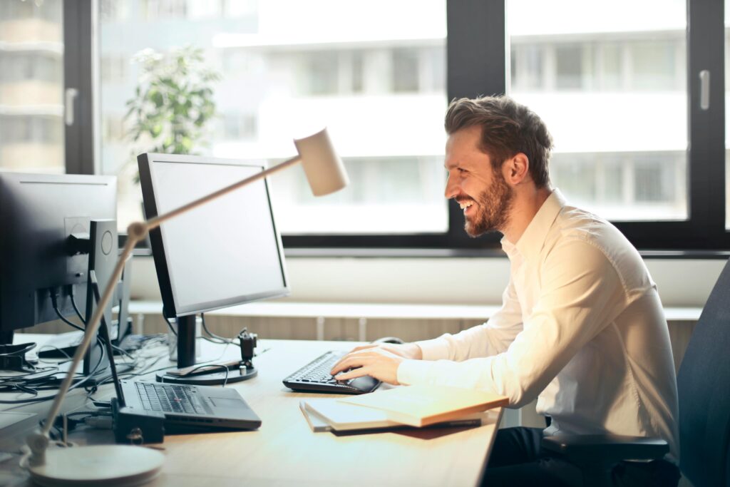 A man in a bright office typing on a computer while considering interview questions for office admin roles.