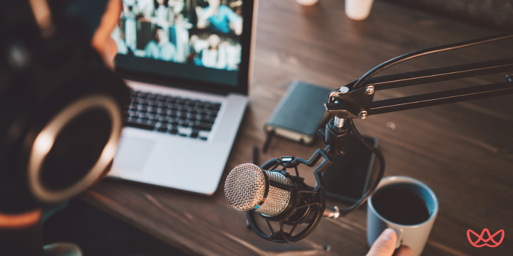 A content creator assistant working on a podcast setup with a microphone, laptop, and coffee cup on a wooden desk.