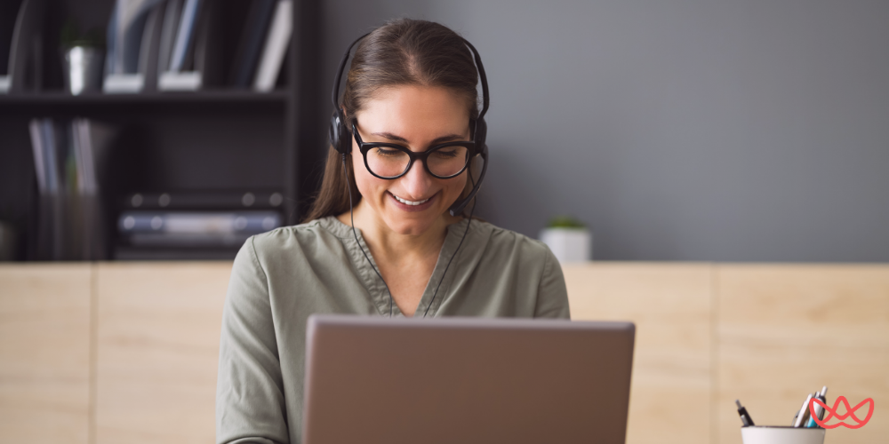 A smiling woman wearing a headset while working on her laptop, representing a freelance business assistant for small and medium businesses.