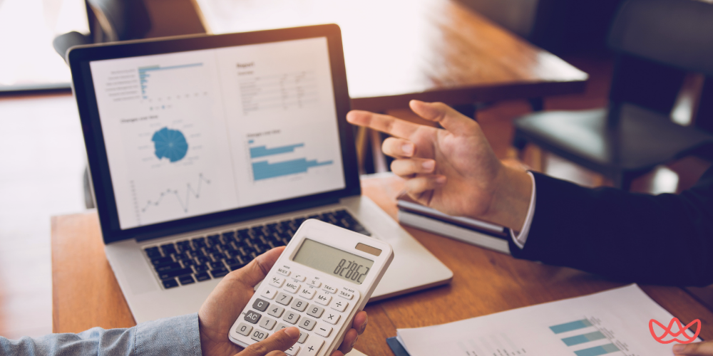 Business professionals analyzing hiring metrics on a laptop with graphs, calculators, and reports, focusing on how to calculate cost per hire.
