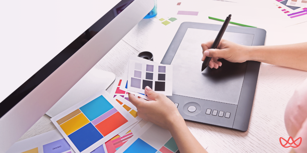 Workspace featuring a digital tablet, color swatches, and a computer, ideal for graphic artist hire projects.