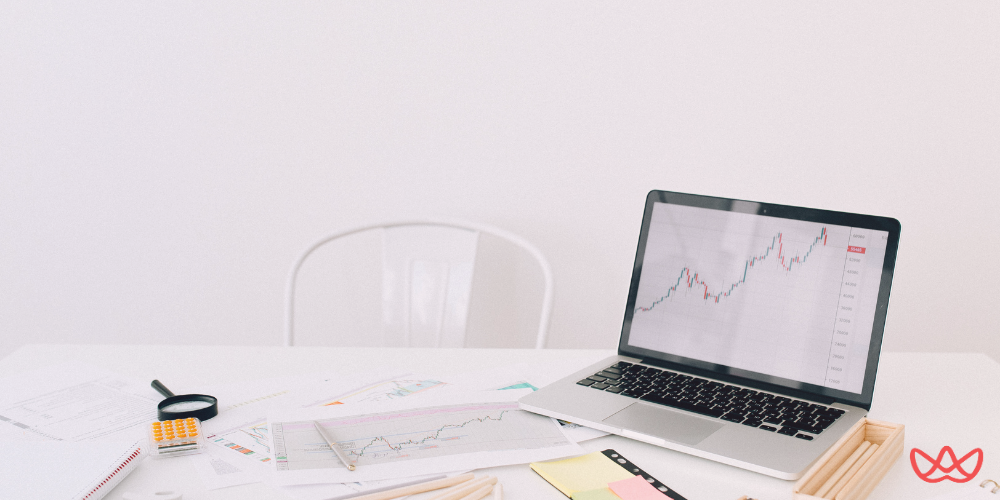 A desk setup with a laptop displaying a marketing analytics graph, surrounded by charts and a magnifying glass, emphasizing the need for a strategic marketing hire to analyze data effectively.