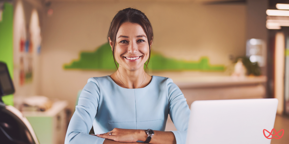 A smiling professional working on her laptop in a modern office, representing a short-term rental virtual assistant.