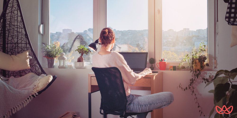 A woman working on her laptop in a sunlit room, illustrating the flexibility and efficiency of a tourism online assistant in managing travel-related tasks remotely.