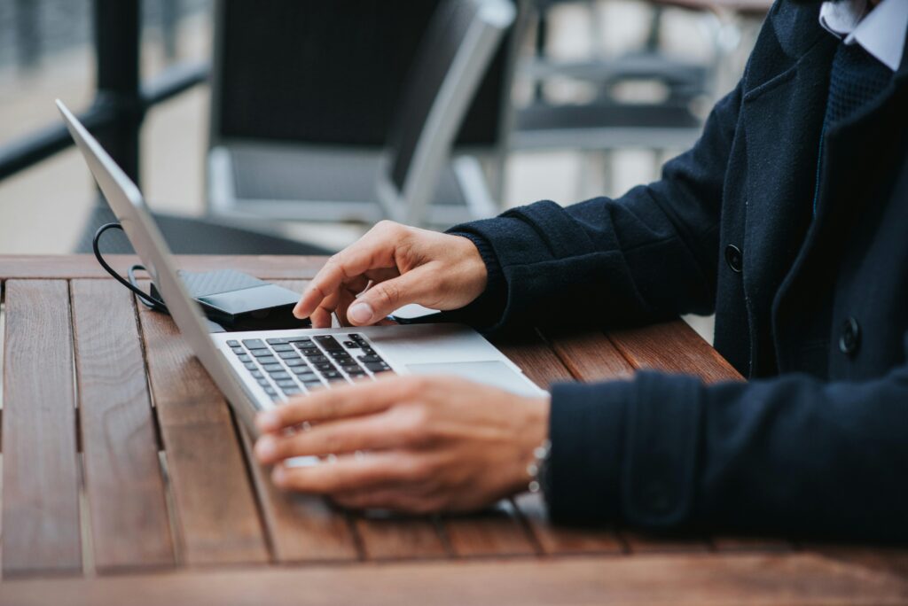 Close-up of hands working on a laptop outdoors, demonstrating the flexibility of outsourcing staff.
