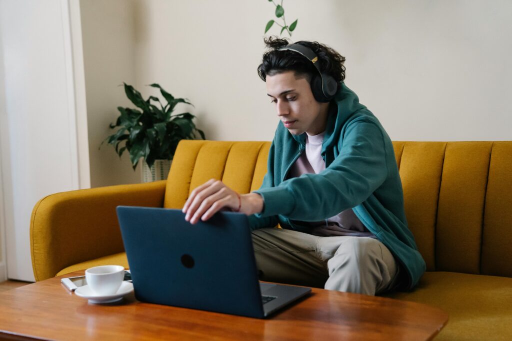A young man wearing headphones while working on his laptop in a casual setting, demonstrating the benefits of a virtual assistant for remote tasks.