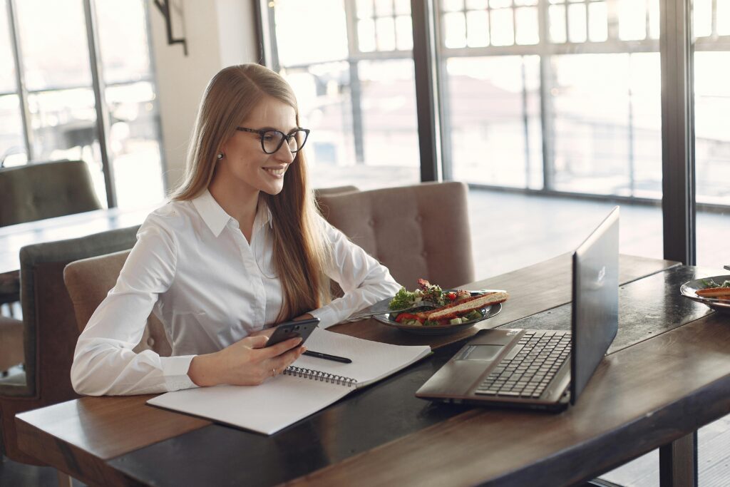 A smiling professional working with a laptop and notes during a meal, showcasing the multitasking ability of a property management virtual assistant.