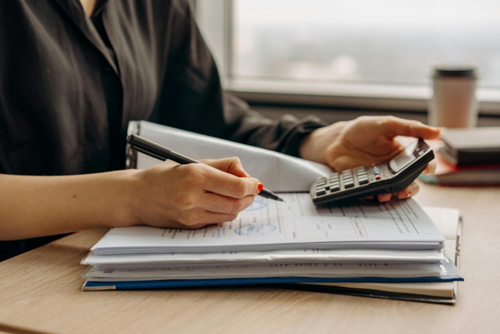 Close-up of a professional using a calculator and reviewing documents to calculate cost per hire.