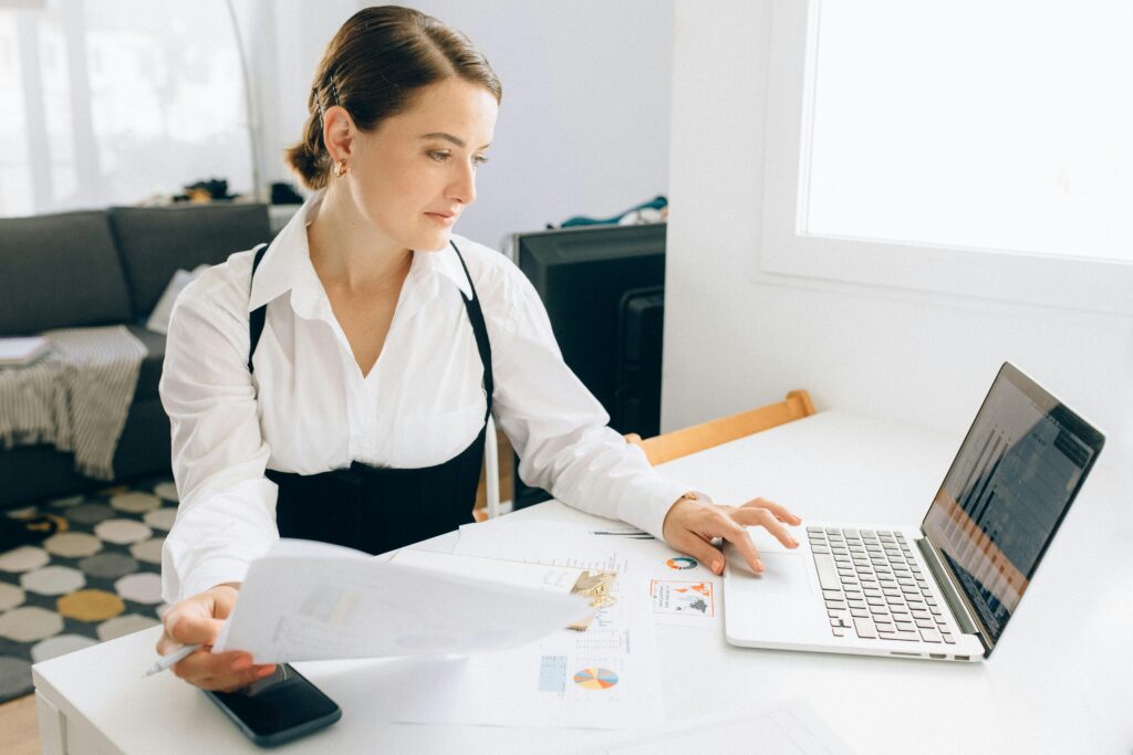 A focused woman reviewing financial documents and working on her laptop, embodying a freelance business assistant for small and medium businesses.