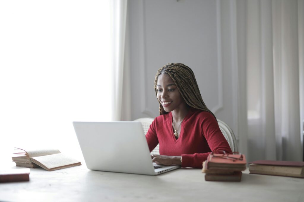 A smiling woman working on her laptop in a cozy setting, representing approachable and skilled executive assistants for hire.