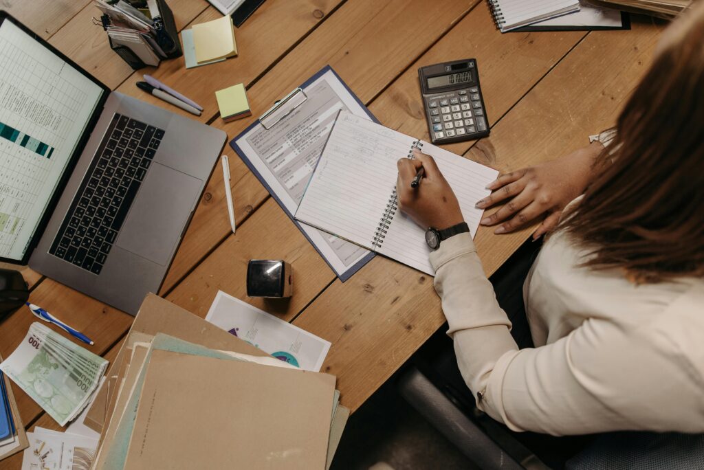 An organized desk with a professional writing in a notebook while reviewing data, representing outsource data entry workflows.