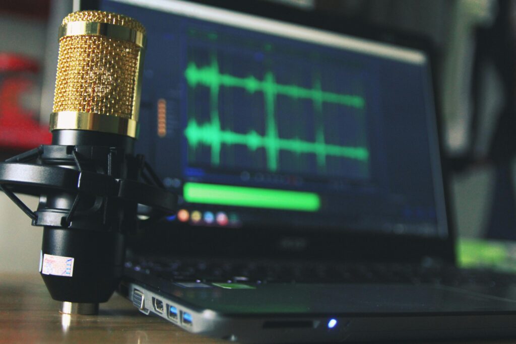 A close-up of a gold microphone and a laptop displaying audio waveforms, symbolizing the technical support of a podcast virtual assistant.