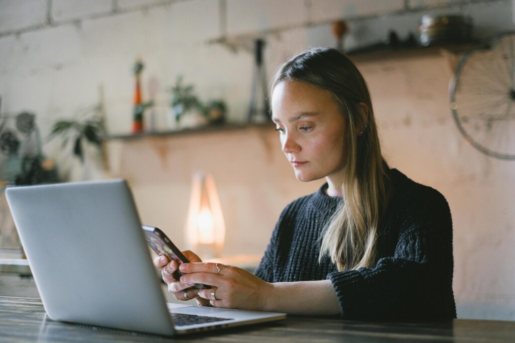 A focused virtual assistant using both a smartphone and laptop, displaying the virtual assistant qualities of tech-savviness and adaptability.