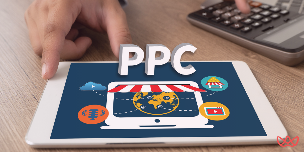 A tablet displaying a digital marketing concept with the text "PPC" prominently featured, surrounded by icons representing various online marketing channels, with a person using a calculator in the background.