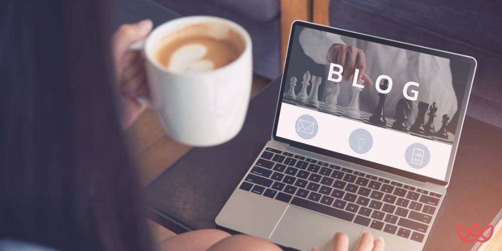 Laptop displaying 'BLOG' interface with chess pieces background and communication icons, alongside a coffee cup, representing blog management workspace.