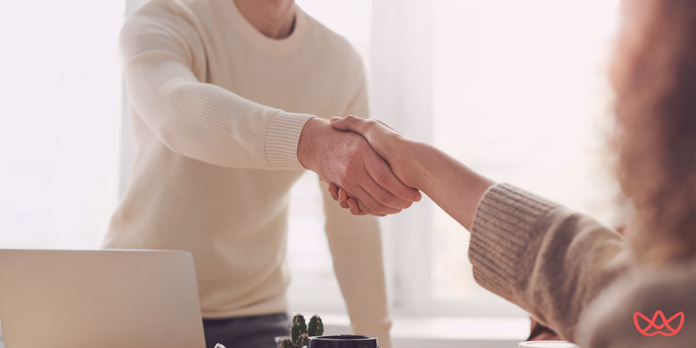 Two individuals shaking hands in an office setting, symbolizing a successful business agreement or partnership, highlighting the client success manager key skills summary.