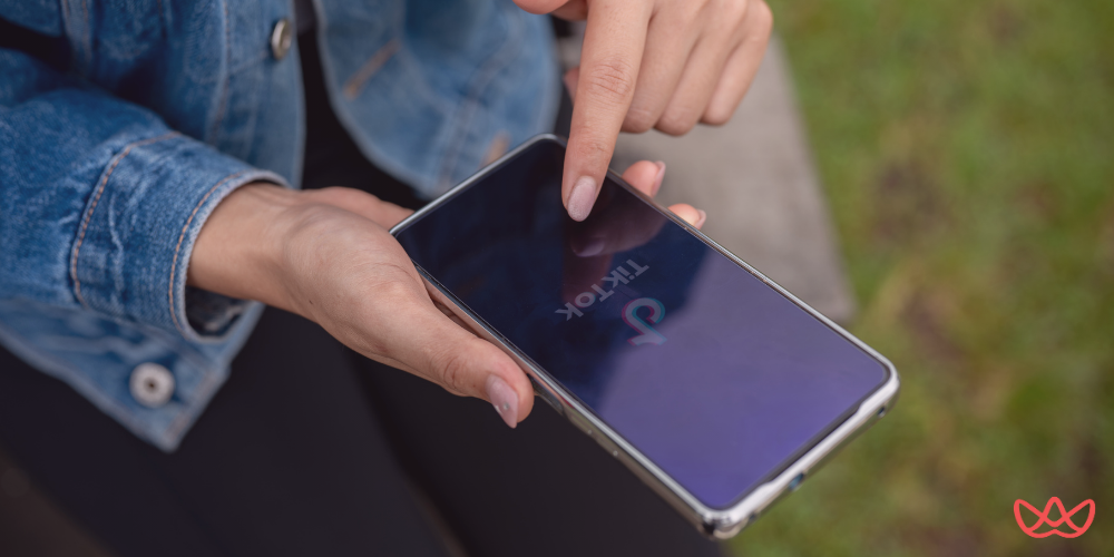 A person wearing a denim jacket is holding a smartphone with the TikTok app open, highlighting the importance of a TikTok growth strategist key skills summary.