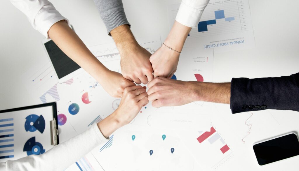 Customer relationship manager (CRM) key skills summary - Five hands coming together in a fist bump over a desk with charts and graphs.