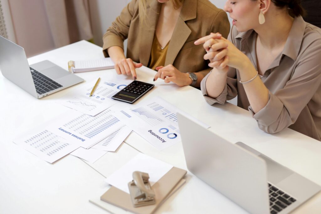 Two professionals working together at a desk with laptops, documents, and a calculator, focusing on an account manager key skills summary report.