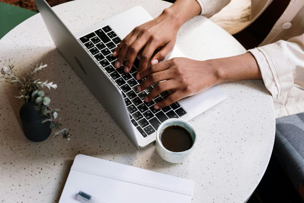 Content marketing manager working on a laptop with a notebook, pen, and coffee cup on a white speckled table, illustrating key skills summary.