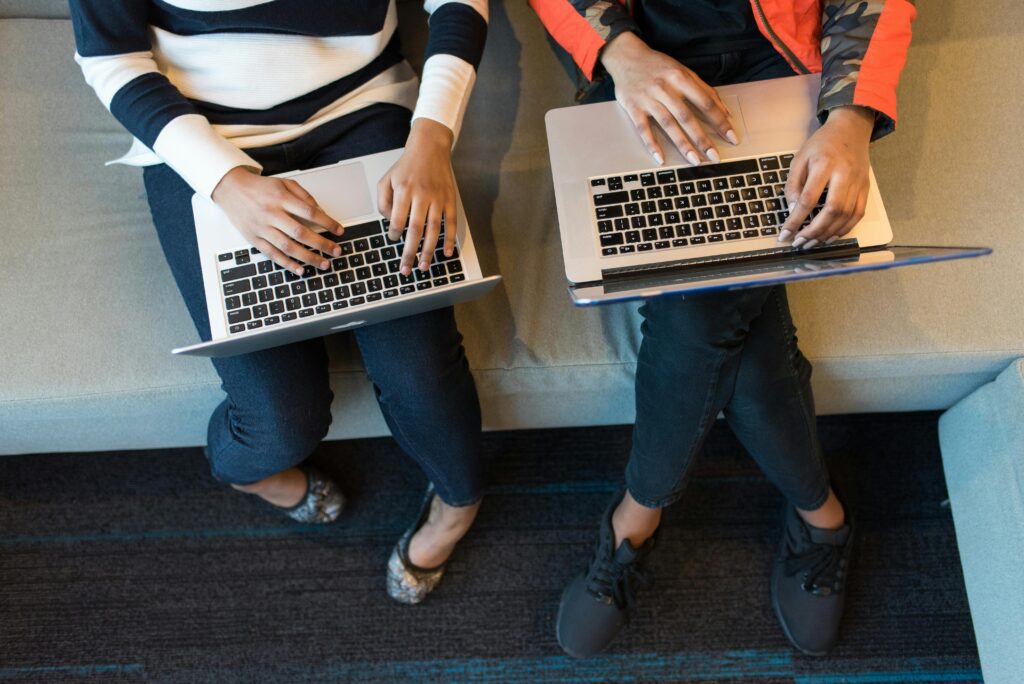 Two individuals sitting on a couch, each working on a laptop, showcasing backend developer key skills summary.