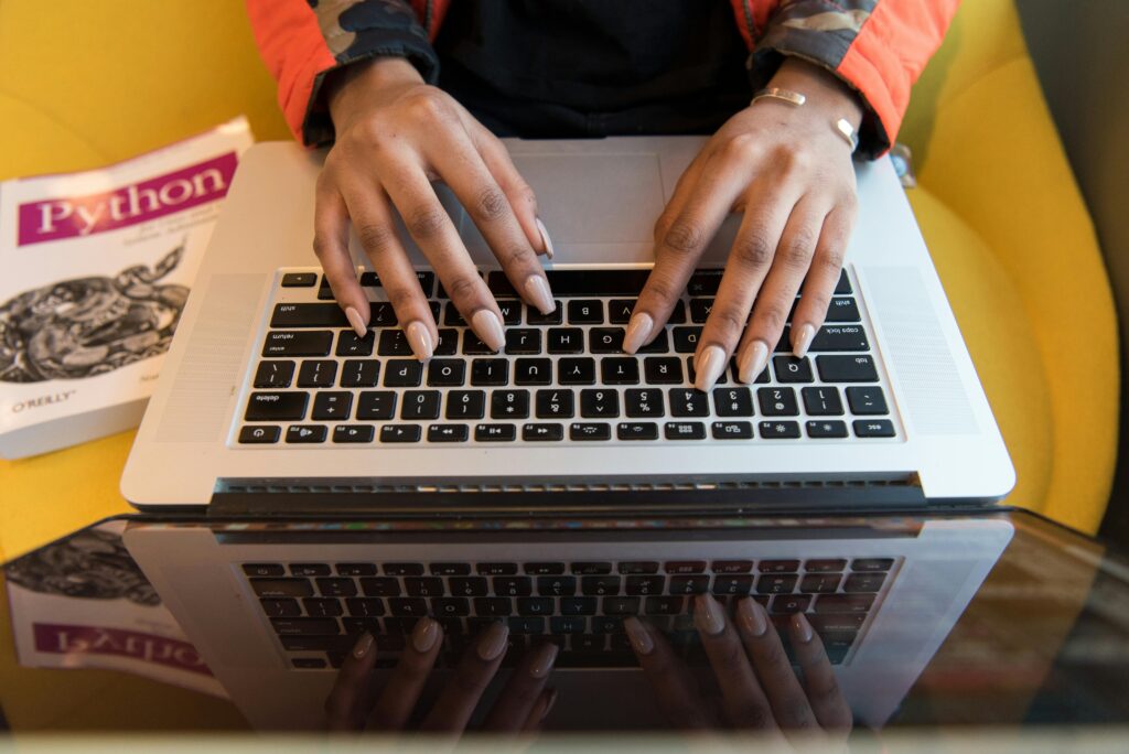 A person typing on a laptop with a Python programming book beside them, illustrating the full-stack developer key skills summary.