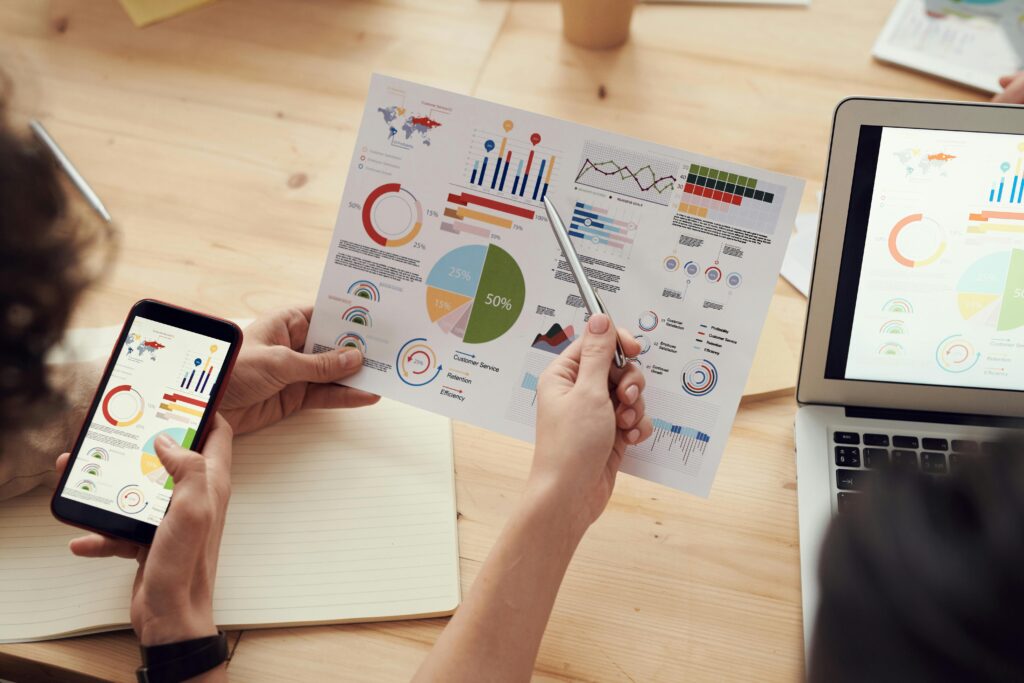 Two people reviewing a printed document and digital screens displaying various colorful charts and graphs, illustrating an agile project manager key skills summary.