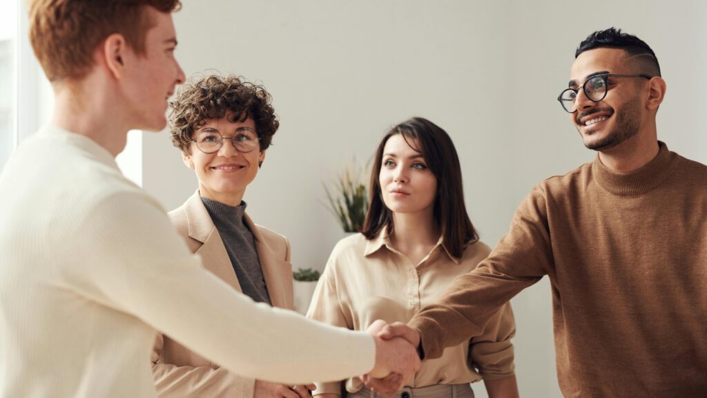 A group of four people in a professional setting, with two individuals shaking hands, symbolizing a successful business agreement or partnership.