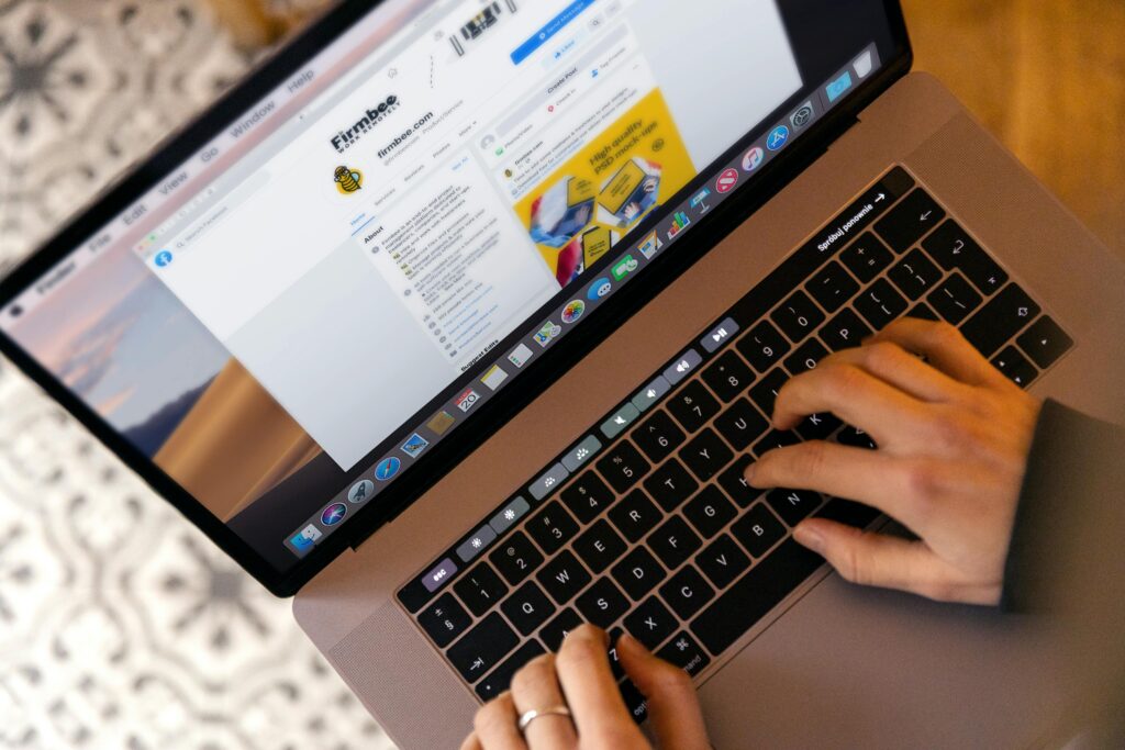A person typing on a MacBook laptop, browsing a social media page related to marketing. The screen displays a business profile, highlighting aspects relevant to an Email Marketing Copywriter Key Skills Summary.