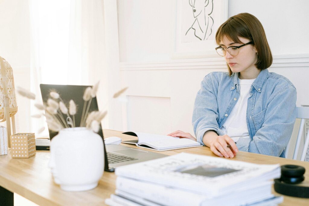A blog manager working at a desk with a laptop, open notebook, and various office supplies, demonstrating key skills in organization and multitasking.