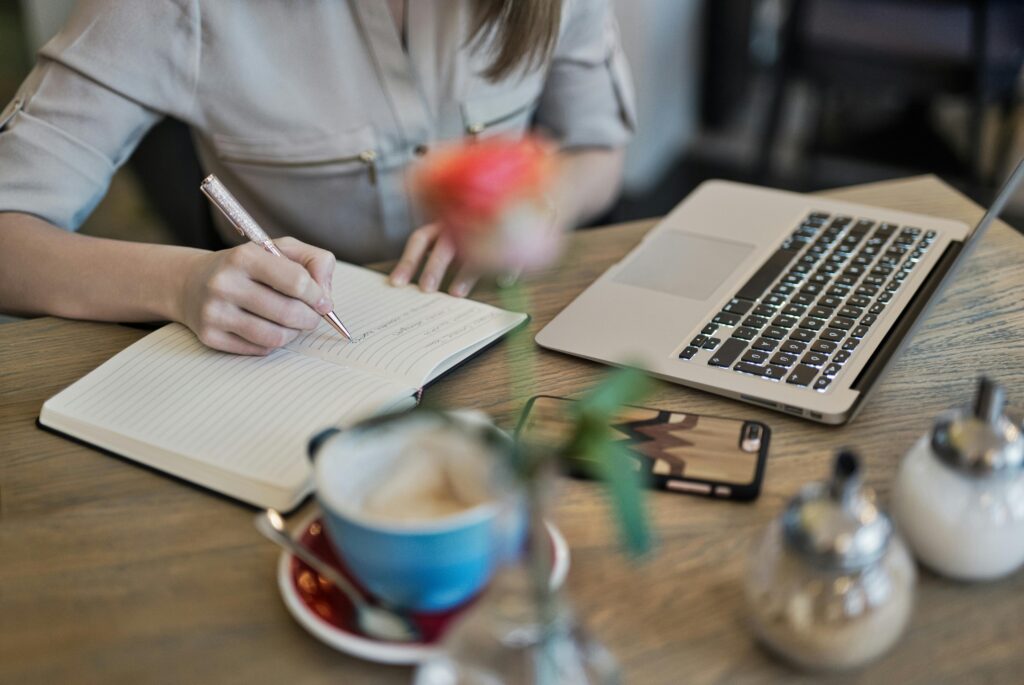 Close-up of hands typing on a laptop keyboard with a document titled "How to Write" visible on the screen, illustrating content writer key skills summary in action. Books and a notebook are visible in the background.