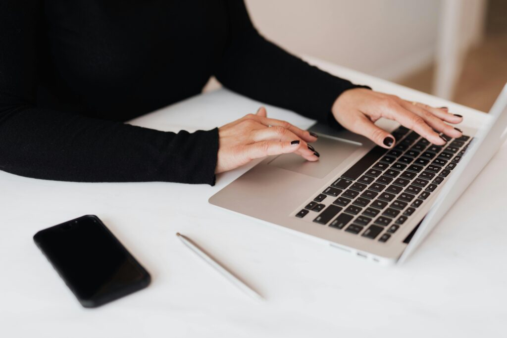 Hands typing on a laptop with a phone and pen nearby, illustrating the focused work environment of a copywriter key skills summary.