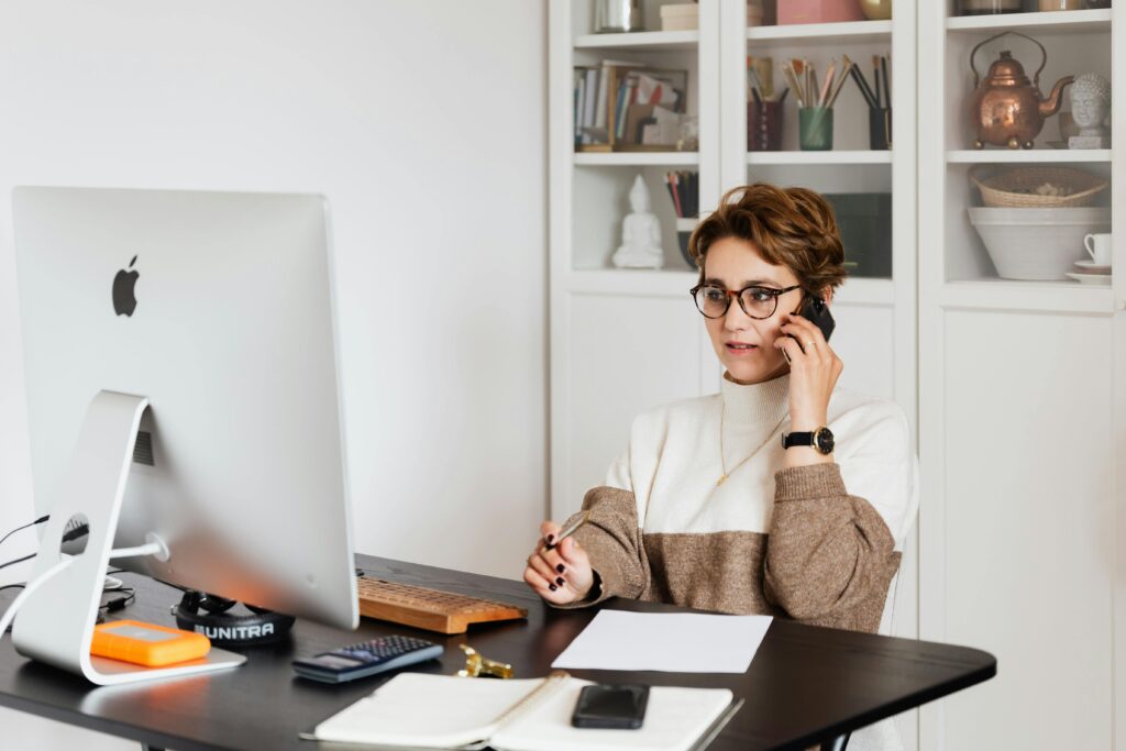 A client success manager key skills summary is demonstrated by a person working at a desk with a computer, taking notes, and talking on the phone.