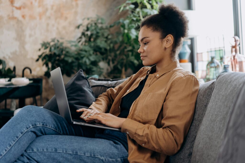 A person sitting on a couch working on a laptop, representing a growth marketing manager key skills summary.
