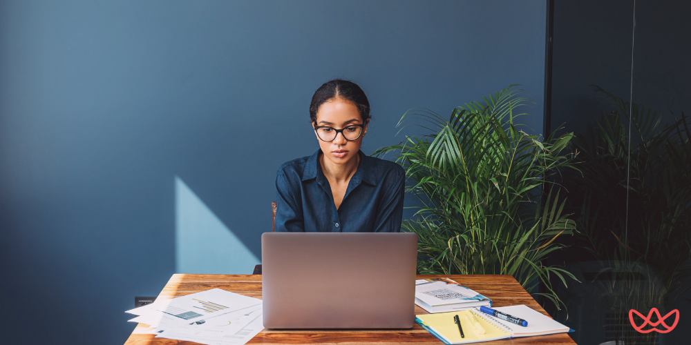 SEO specialist analyzing charts and graphs on a laptop at a desk adorned with documents and plants.