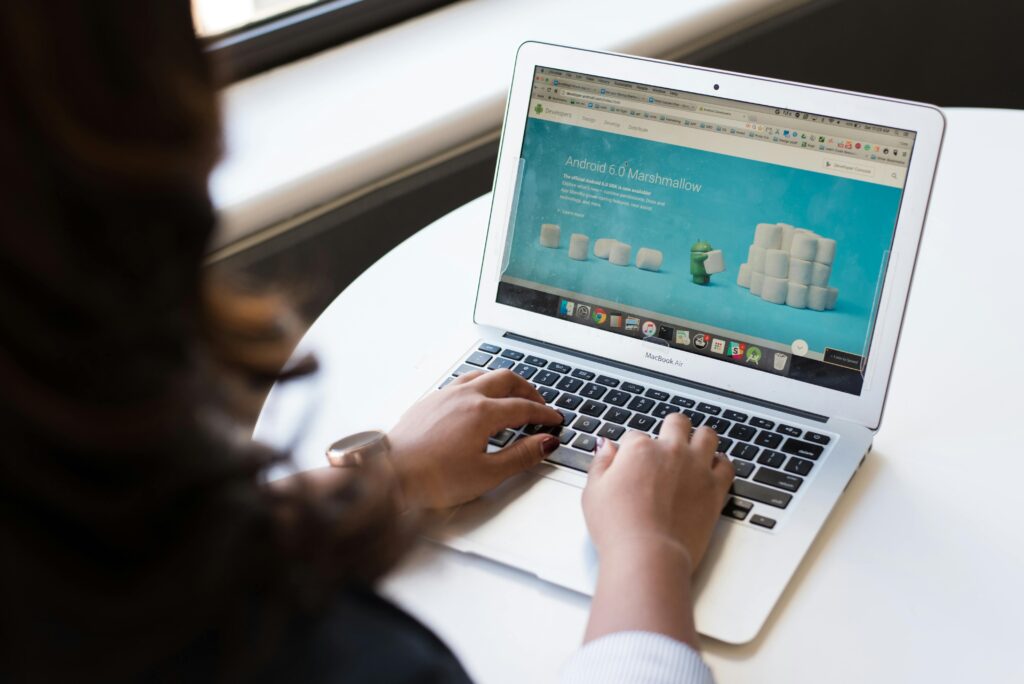 A person typing on a MacBook Air with a webpage about Android 6.0 Marshmallow visible, illustrating a WordPress developer key skills summary in a professional setup.