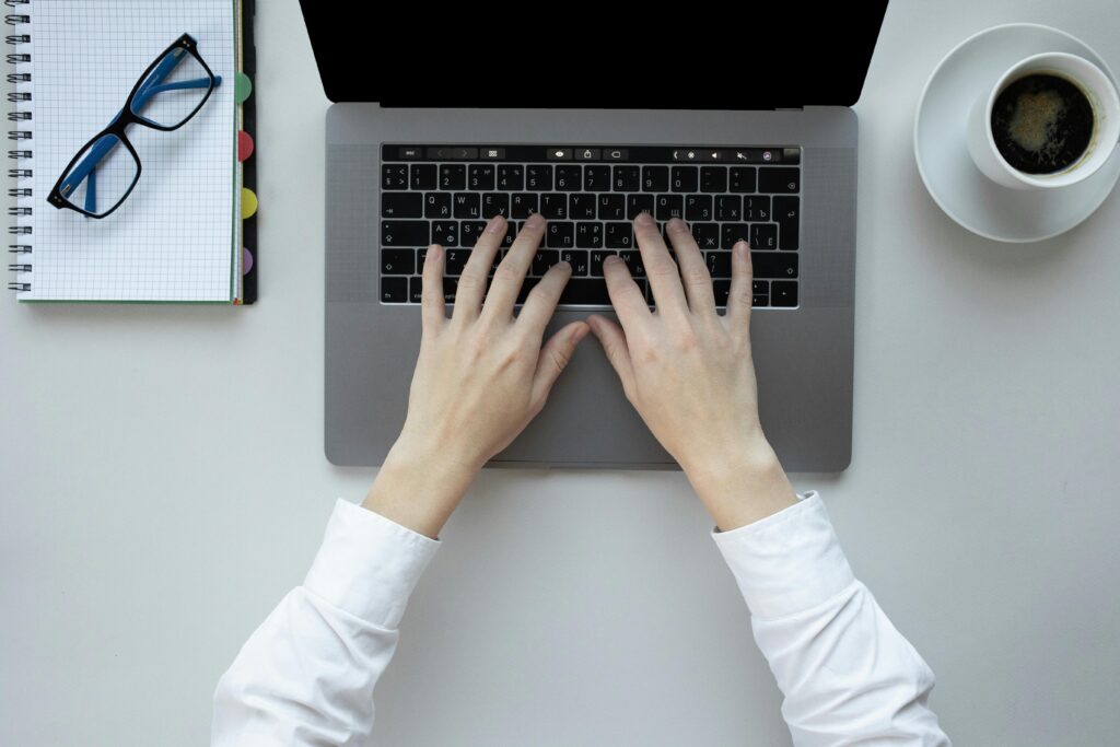 Hands typing on a laptop keyboard with a notebook, glasses, and a cup of coffee nearby, illustrating a Klaviyo expert key skills summary.