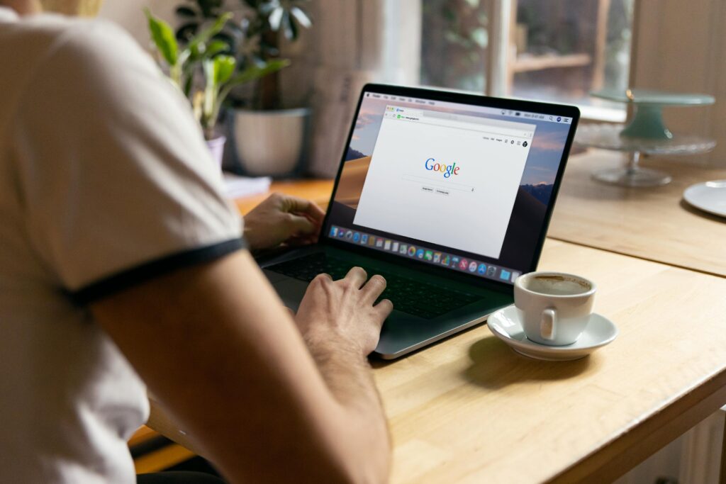 A person working on a laptop with the Google search page open, accompanied by a cup of coffee on the table and a small potted plant in the background, representing the Programmatic Ads Specialist Key Skills Summary.