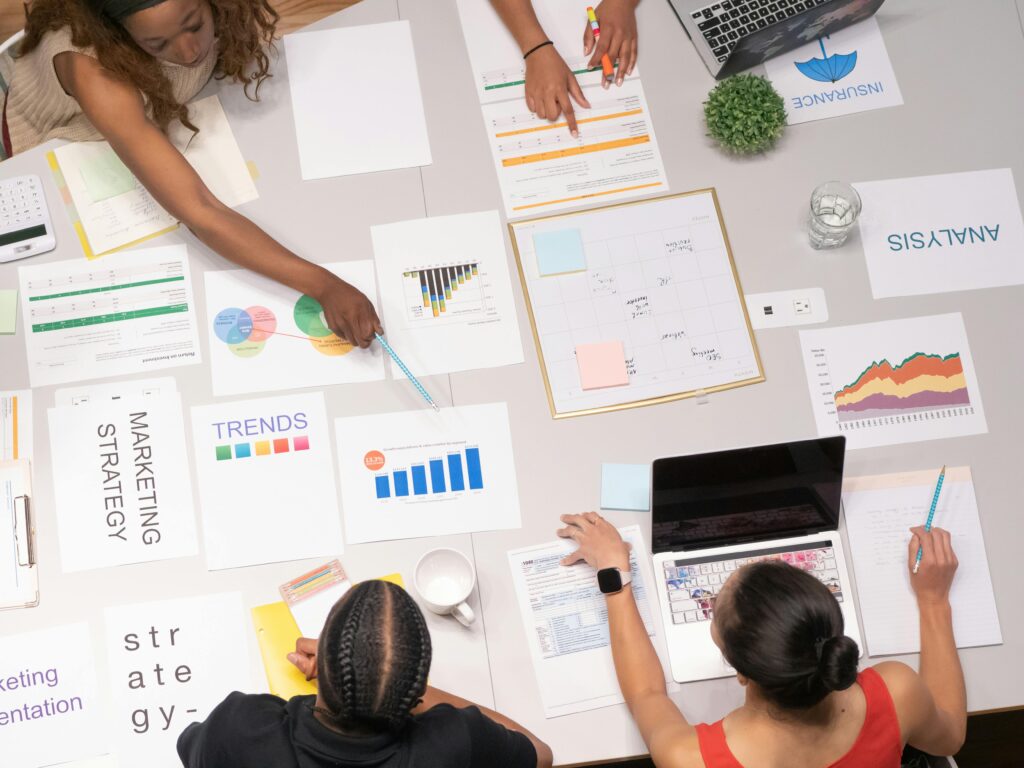 A group of professionals collaborating around a table with documents, charts, and laptops, illustrating an SEO analyst key skills summary.