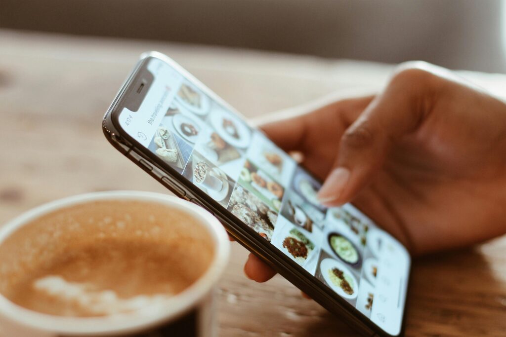 A smartphone displaying a grid of vibrant food images, set on a table next to a cup of coffee, embodying the social media manager key skills summary.