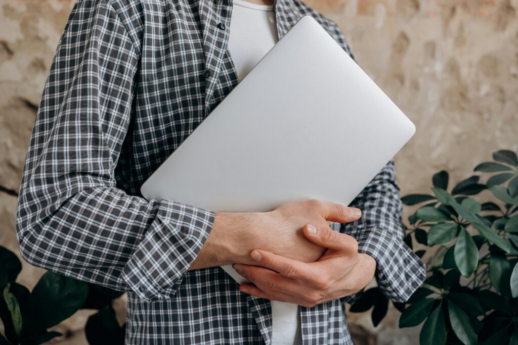 A person in a checkered shirt holding a closed laptop, representing the performance marketing director key skills summary.