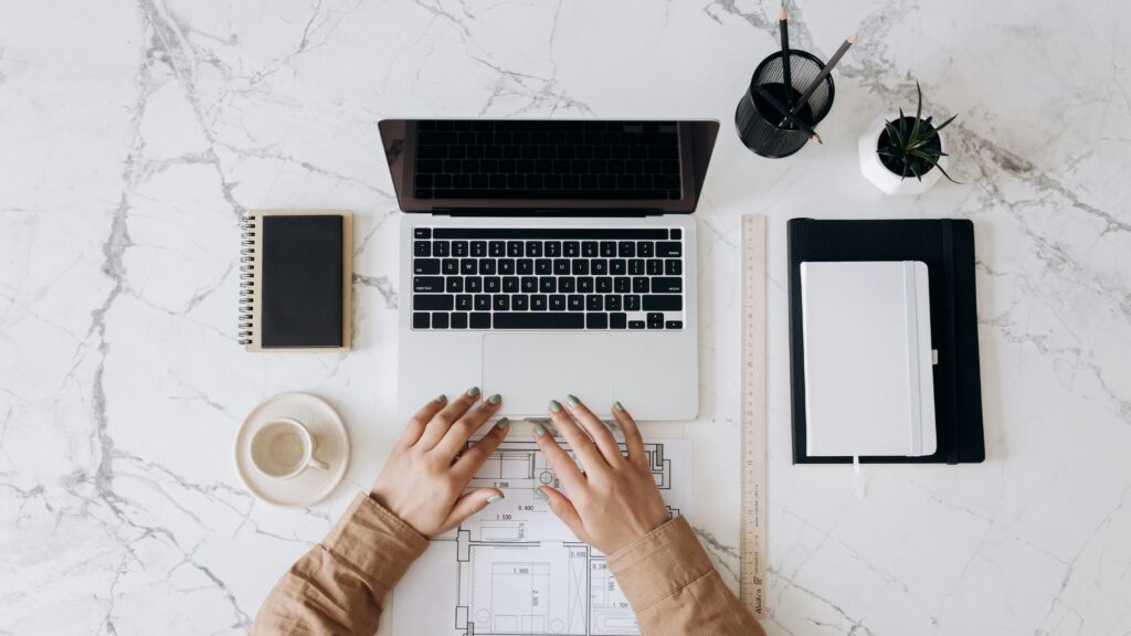 Marketplace growth strategist key skills summary workspace with a laptop, architectural plans, notebooks, and office supplies on a marble desk.
