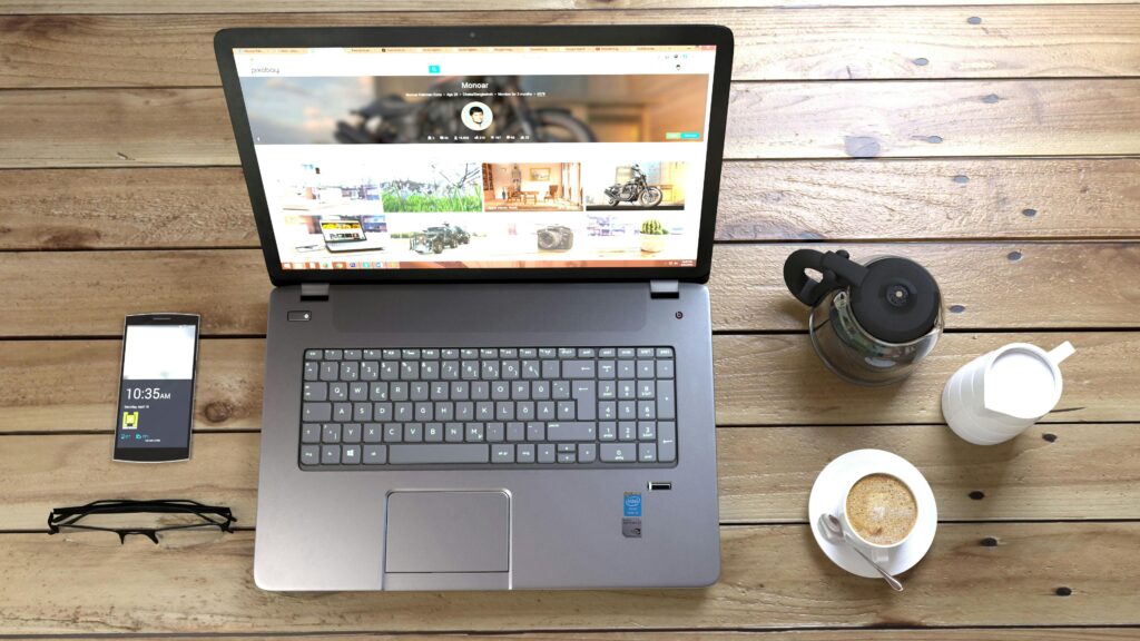 A laptop on a wooden table, displaying a webflow developer key skills summary, accompanied by a smartphone, eyeglasses, a coffee cup, a coffee pot, and a milk jug.