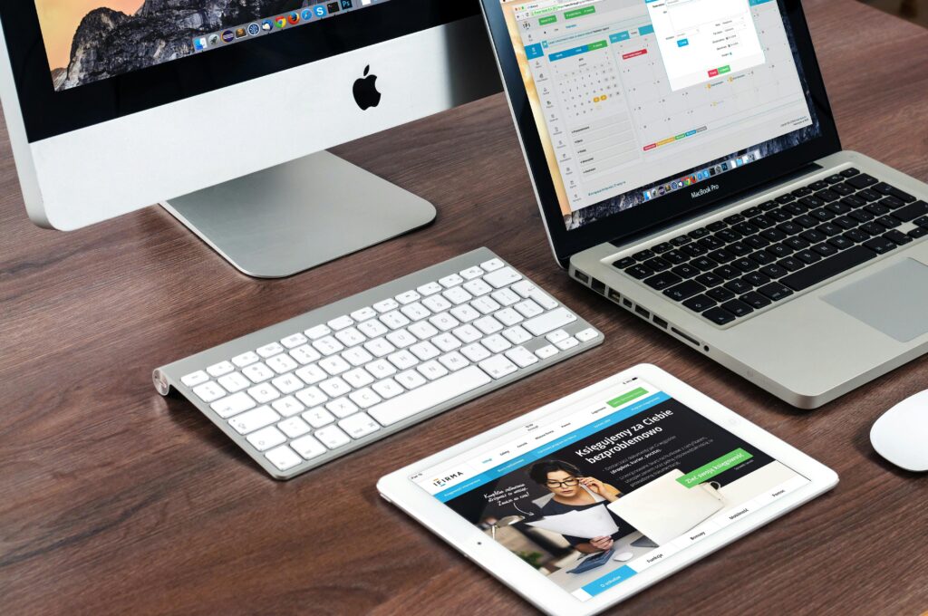 A workspace featuring an iMac, MacBook Pro, and iPad, with the iPad displaying a web designer key skills summary alongside design-related tools.